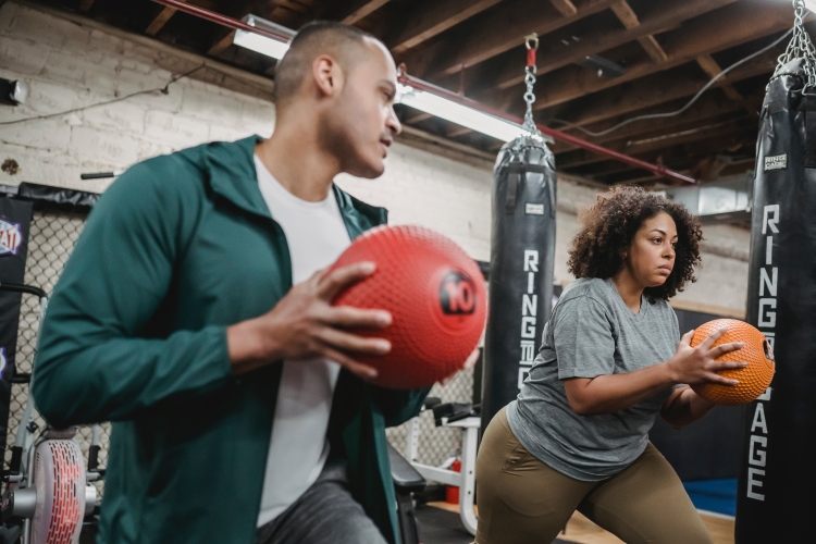 A woman holding an exercise ball being coached by a man